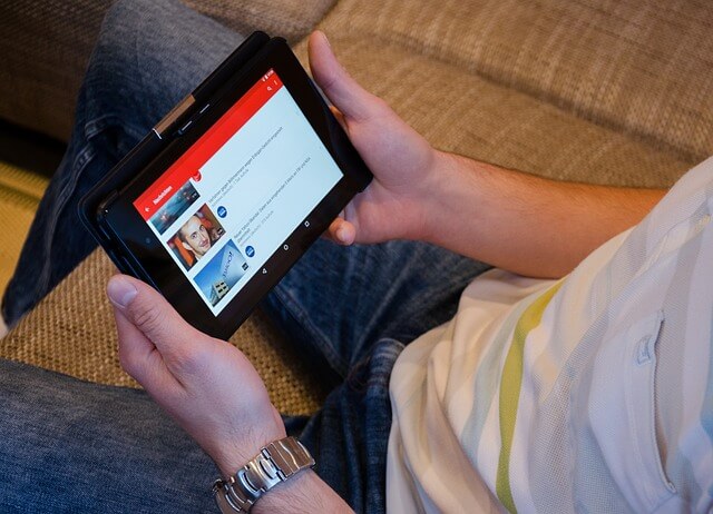 A man sitting on a couch watching YouTube videos on his tablet