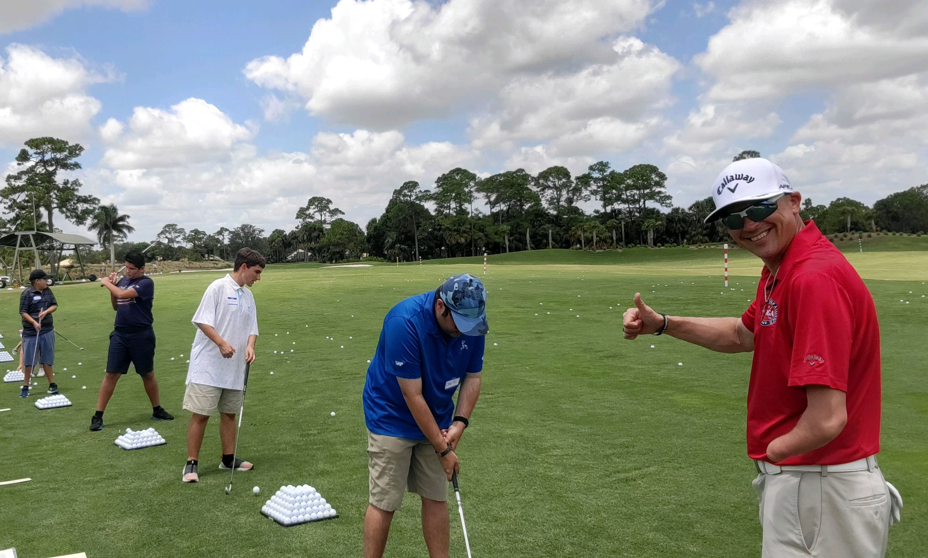 a group of golfers with disabilities and their coach on the course hitting balls