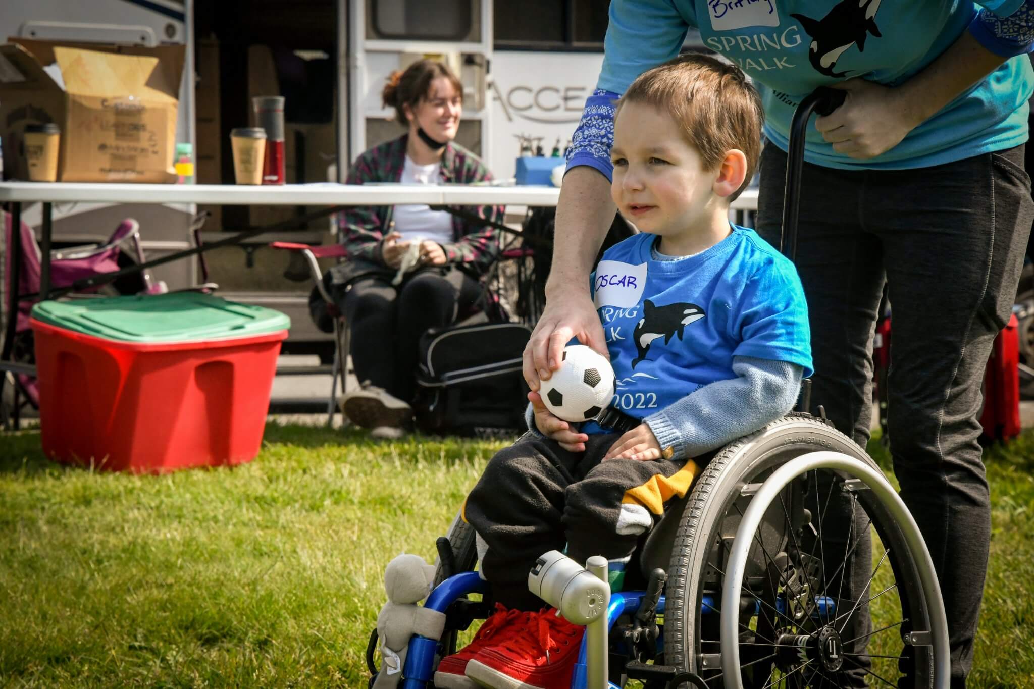 Young boy in a wheelchair is outside on a field and being handed a soccer ball