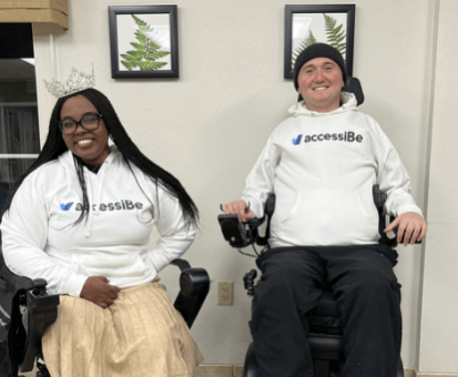 Chandra Smith, Ms. Wheelchair America 2024, and Josh Basile, accessiBe's Community Relations Manager, sitting in their power wheelchairs and wearing accessiBe swag at an adaptive skiing event.