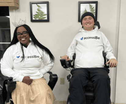 Chandra Smith, Ms. Wheelchair America 2024, and Josh Basile, accessiBe's Community Relations Manager, sitting in their power wheelchairs and wearing accessiBe swag at an adaptive skiing event.