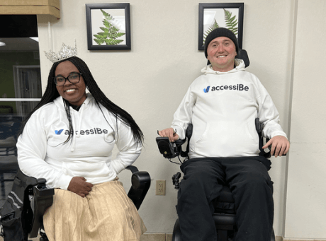 Chandra Smith, Ms. Wheelchair America 2024, and Josh Basile, accessiBe's Community Relations Manager, sitting in their power wheelchairs and wearing accessiBe swag at an adaptive skiing event.